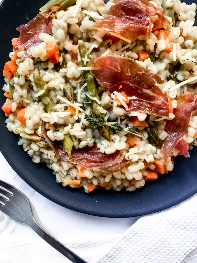 barley risotto with asparagus and crispy prosciutto on a dark plate with a fork
