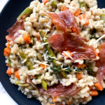 barley risotto with asparagus and crispy prosciutto on a dark plate