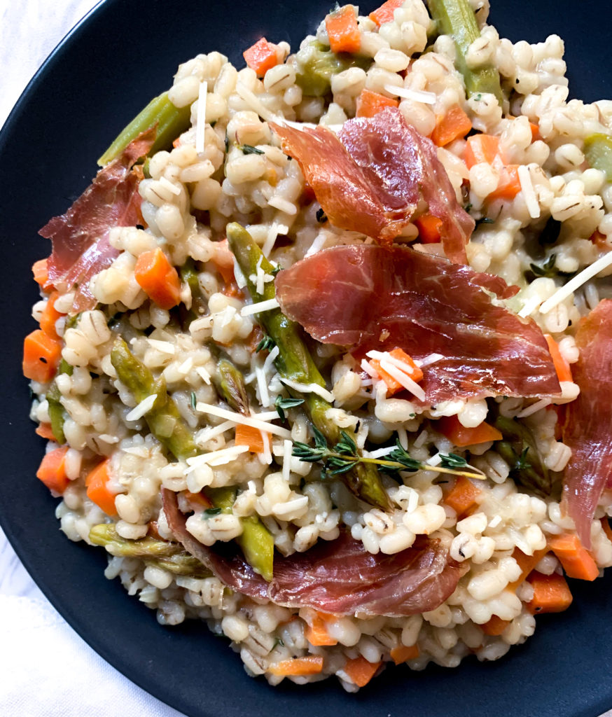 barley risotto with asparagus and crispy prosciutto on a dark plate