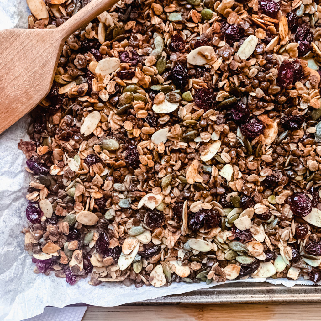 maple cinnamon lentil granola on baking sheet with a wooden spatula