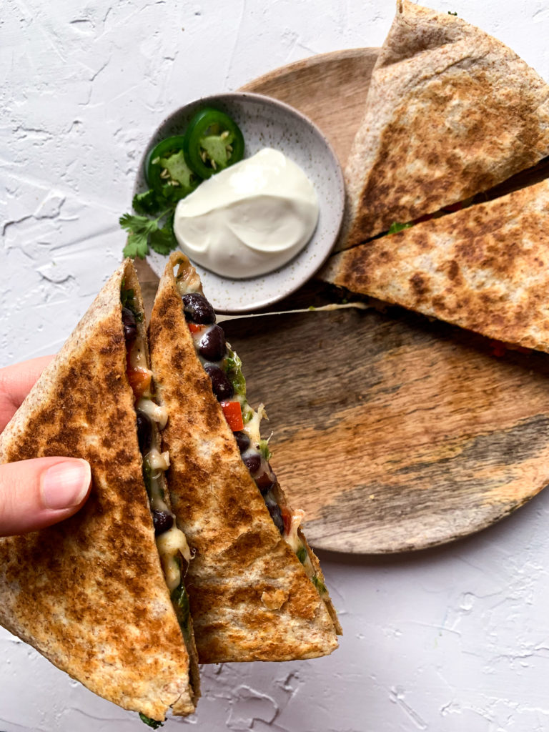 hand holding two pieces of black bean and kale quesadillas with a cheese pull