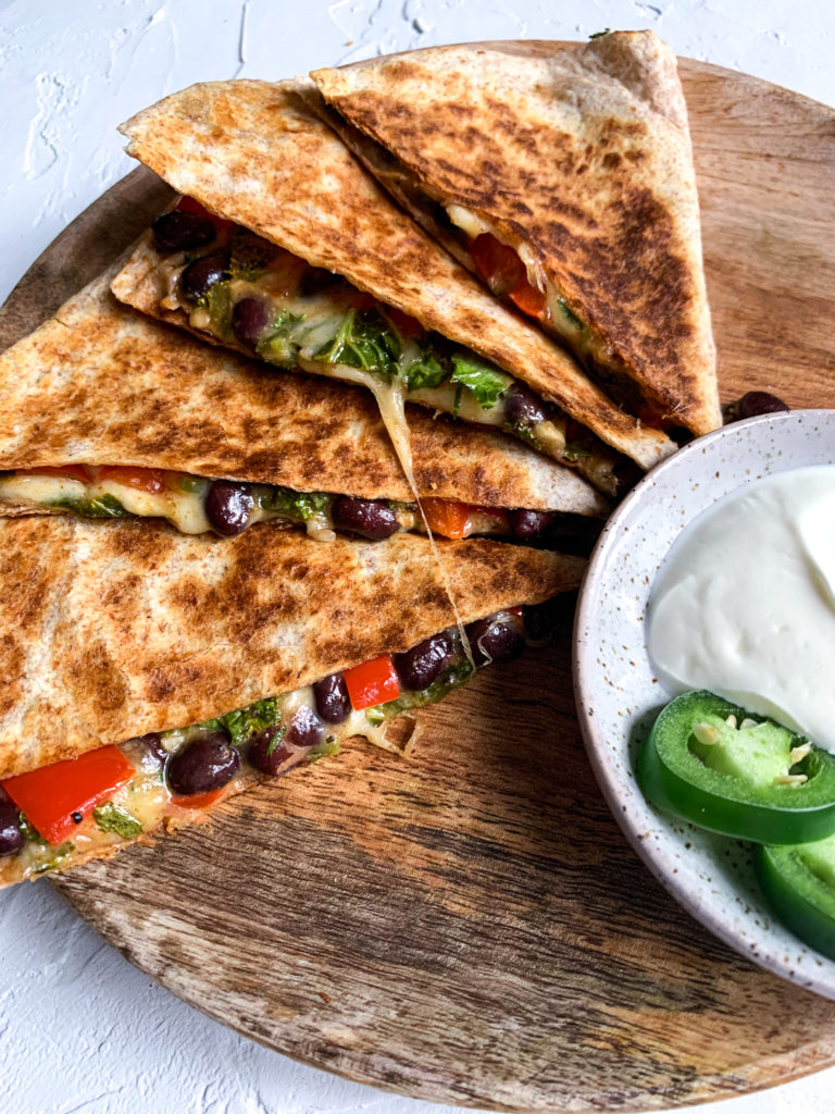 close up of black bean and kale quesadillas slices layered over one another on a wooden plate