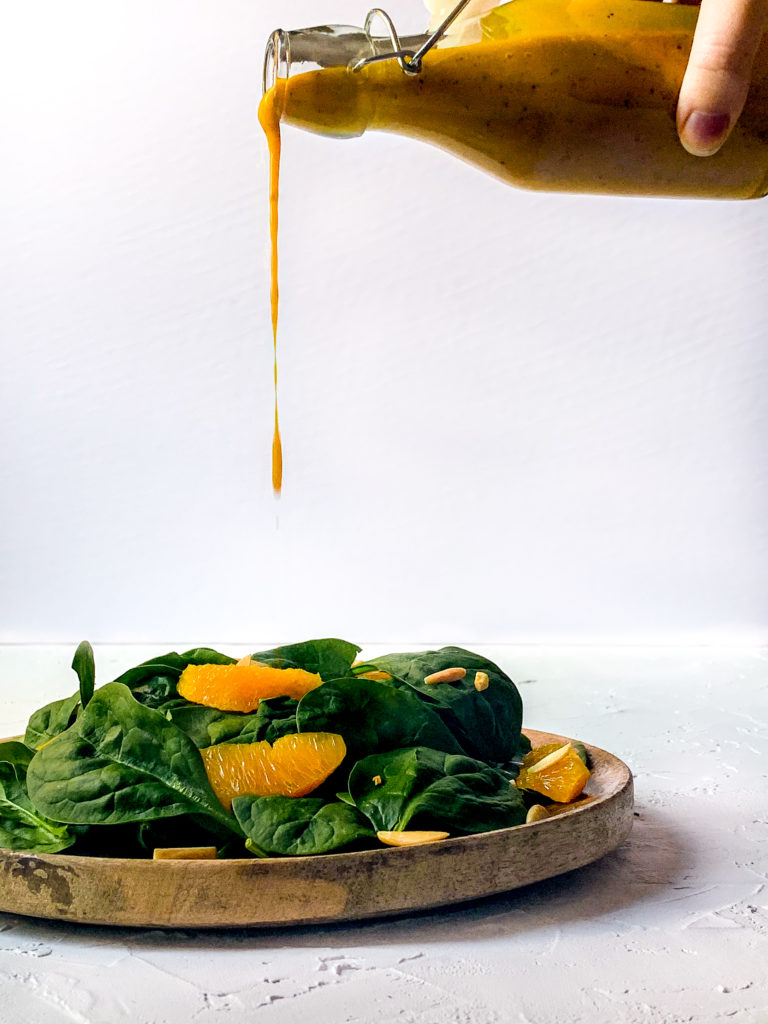 homemade mango chutney vinaigrette being poured over a spinach salad on a white background