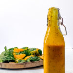 close up of homemade mango chutney vinaigrette with spinach salad in front of white background