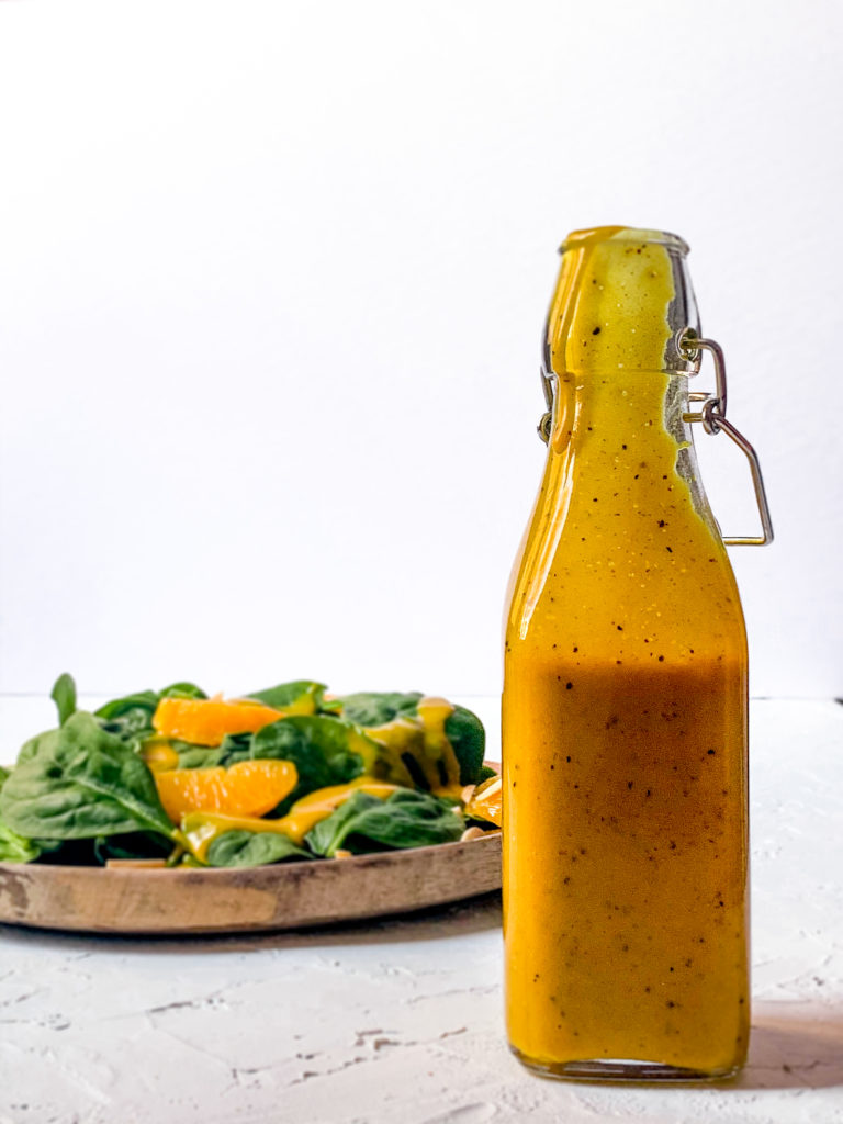 close-up shot of homemade mango chutney vinaigrette in a glass bottle with a spinach salad in the background