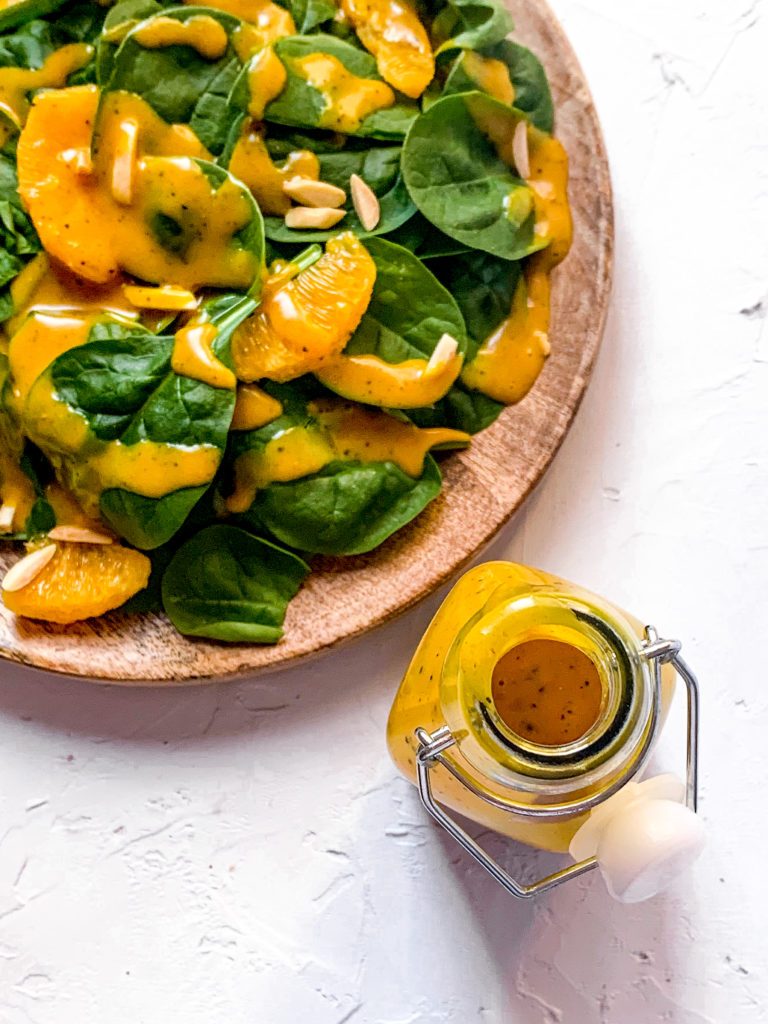 overhead shot of a spinach salad and vinaigrette bottle on white surface