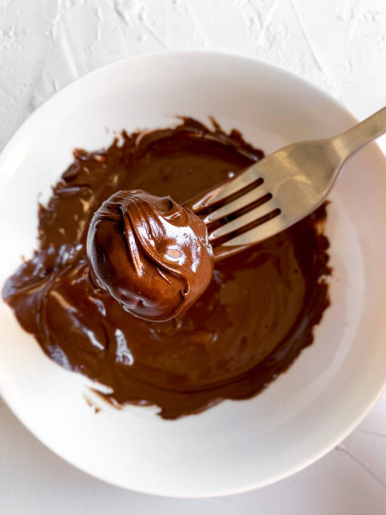 chocolate peanut butter date caramel ball being dipped in bowl of chocolate on a fork