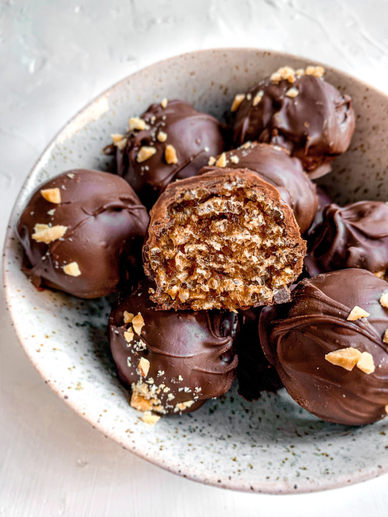 close up of chocolate peanut butter date caramel ball cut in half among a bowl of others