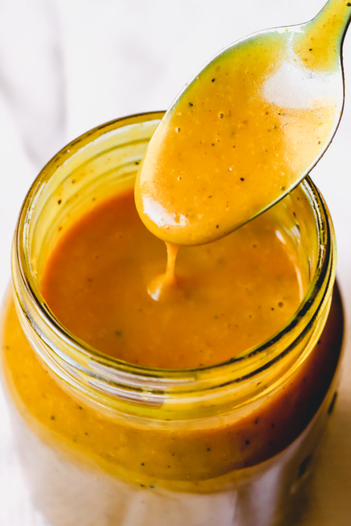 mango chutney vinaigrette dripping off spoon into a jar