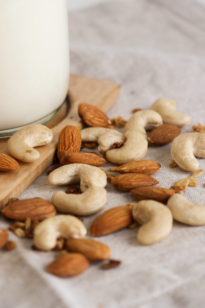 almonds and cashews on canvas with glass of non-dairy milk