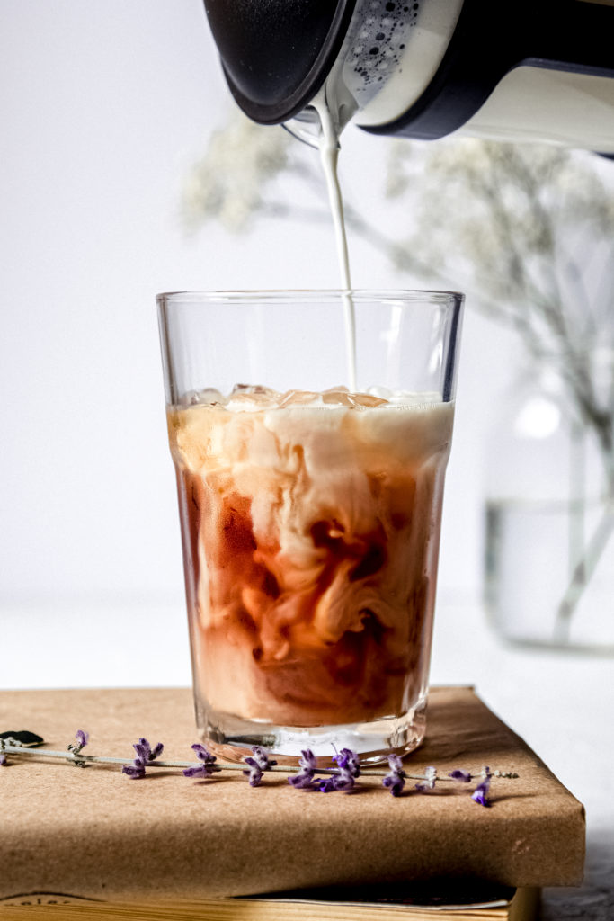 cold foamed milk being poured over a glass of iced tea.