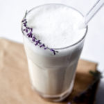 Iced Earl Grey Latte with Easy Vanilla Cold Foam in a glass jar with a straw and purple flower garnish.