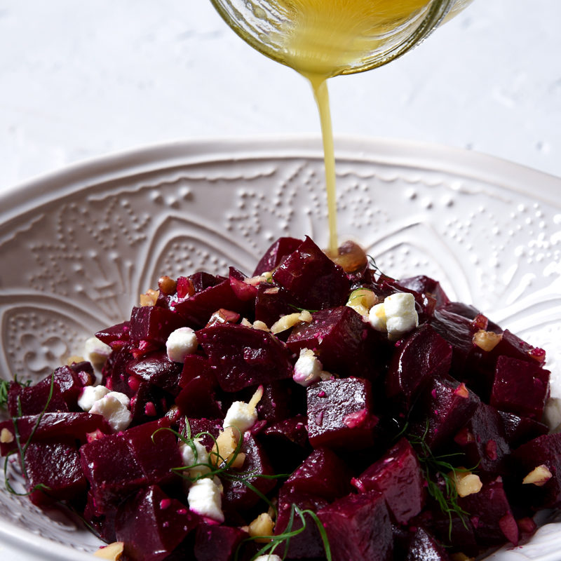 beet salad in a white bowl with simple citrus dressing being poured on top