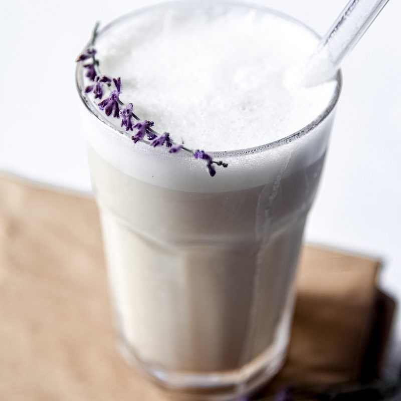 Iced Earl Grey Latte with Easy Vanilla Cold Foam in a glass jar with a straw and purple flower garnish.