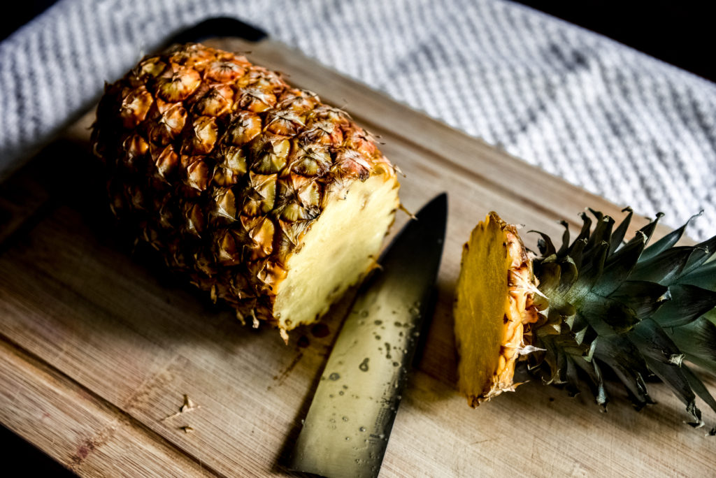 A pineapple with its top removed on a wooden cutting board.