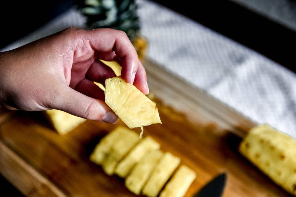 Close-up of a hand holding a chunk of pineapple.