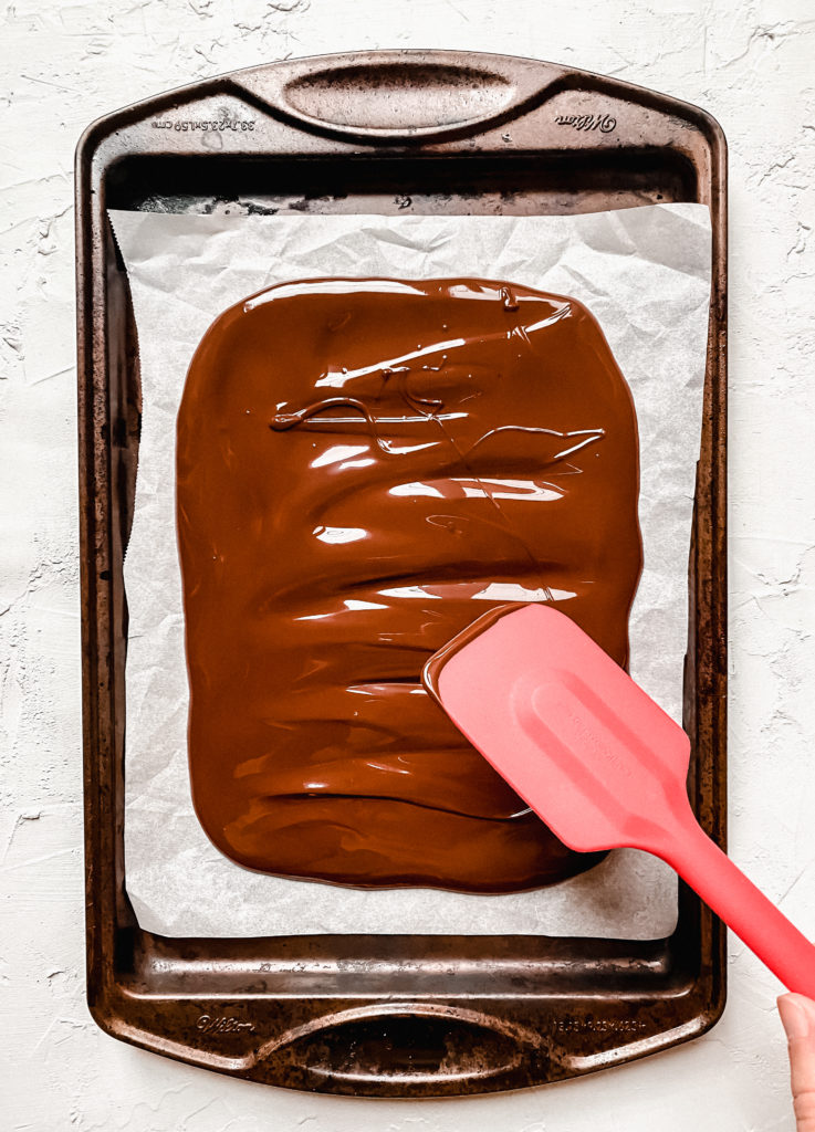 spatula smoothing out chocolate on a baking sheet