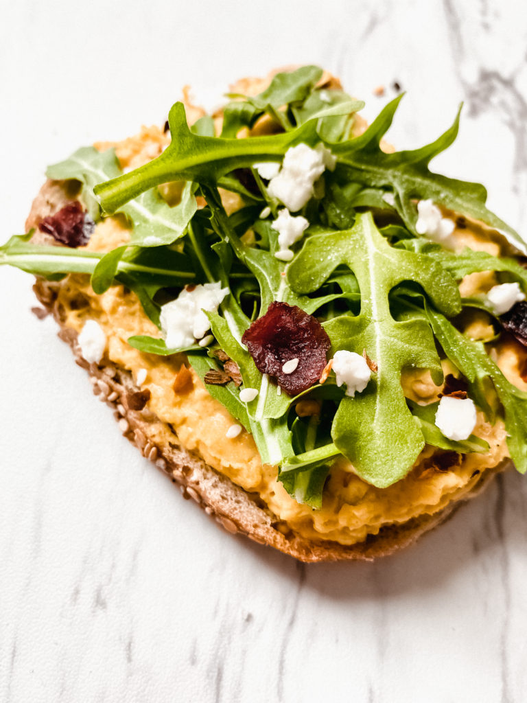 smashed chickpea salad toasts topped with arugula, feta and dried cranberries