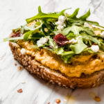 smashed curry chickpeas on toast with arugula and dried cranberries on a marble background