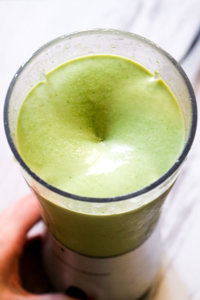 overhead shot of a green smoothie swirling in a blender