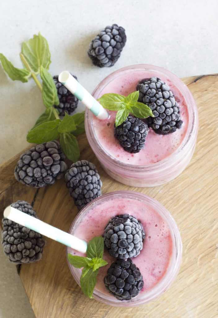 overhead shot of pink protein smoothies in jars with blackberries and mint on a wooden cutting board