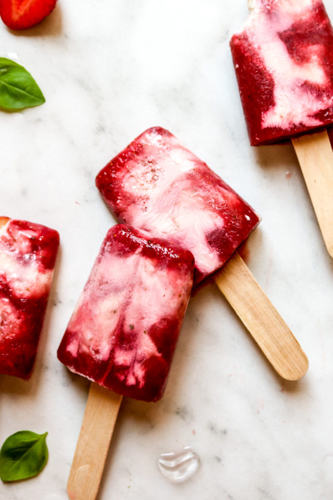 swirled yogurt popsicles on a marble backdrop with ice and basil