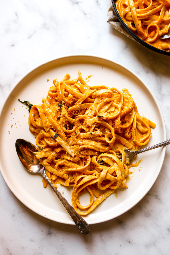 overhead shot of pumpkin alfredo pasta swirled on a fork laying on a plate beside a spoon