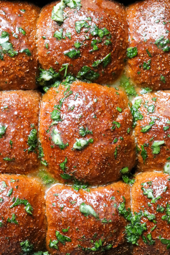 close up of whole wheat molasses dinner rolls topped with garlic parsley butter