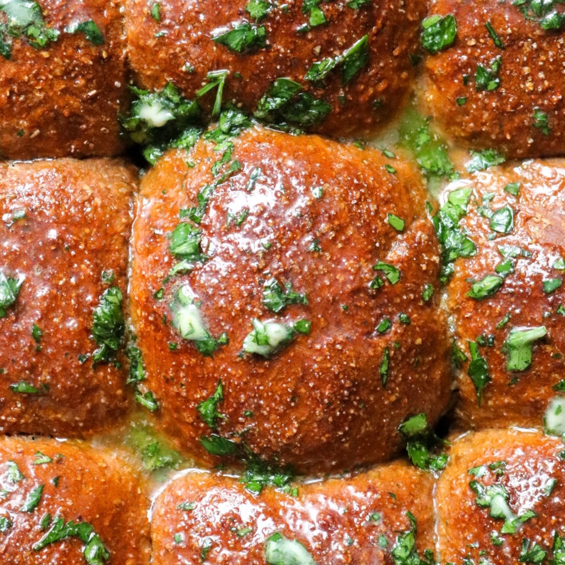 close up of whole wheat molasses dinner rolls topped with herb butter
