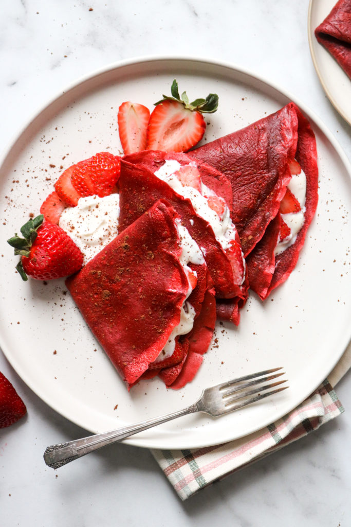 Red velvet crêpes filled with strawberries and cream layered on a plate