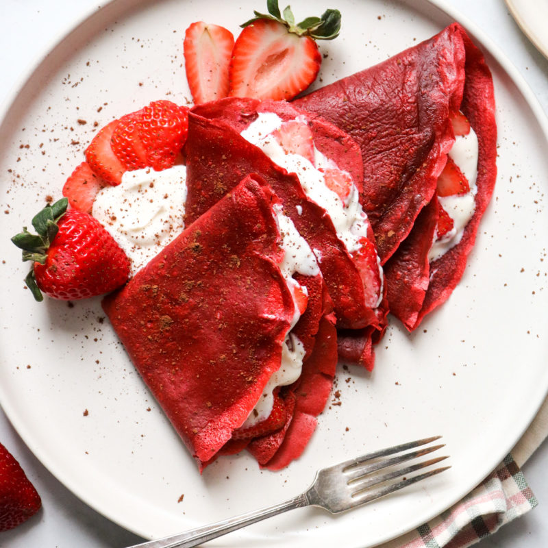 Red velvet crêpes filled with strawberries and cream layered on a plate