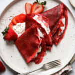 Red velvet crêpes filled with strawberries and cream layered on a plate
