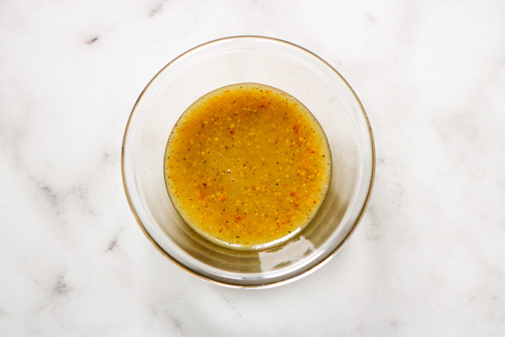 mustard dressing in a small glass bowl on a marble background