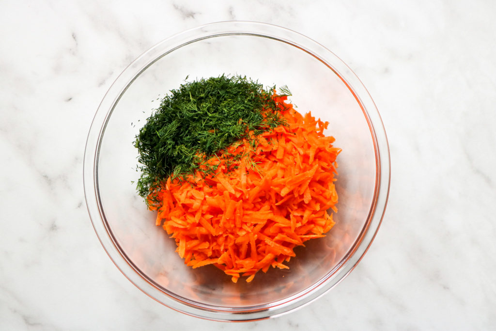 chopped dill and shredded carrots in a glass bowl on a marble background
