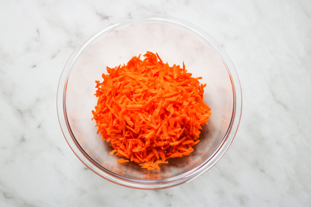 shredded carrots in a large glass bowl on a marble background