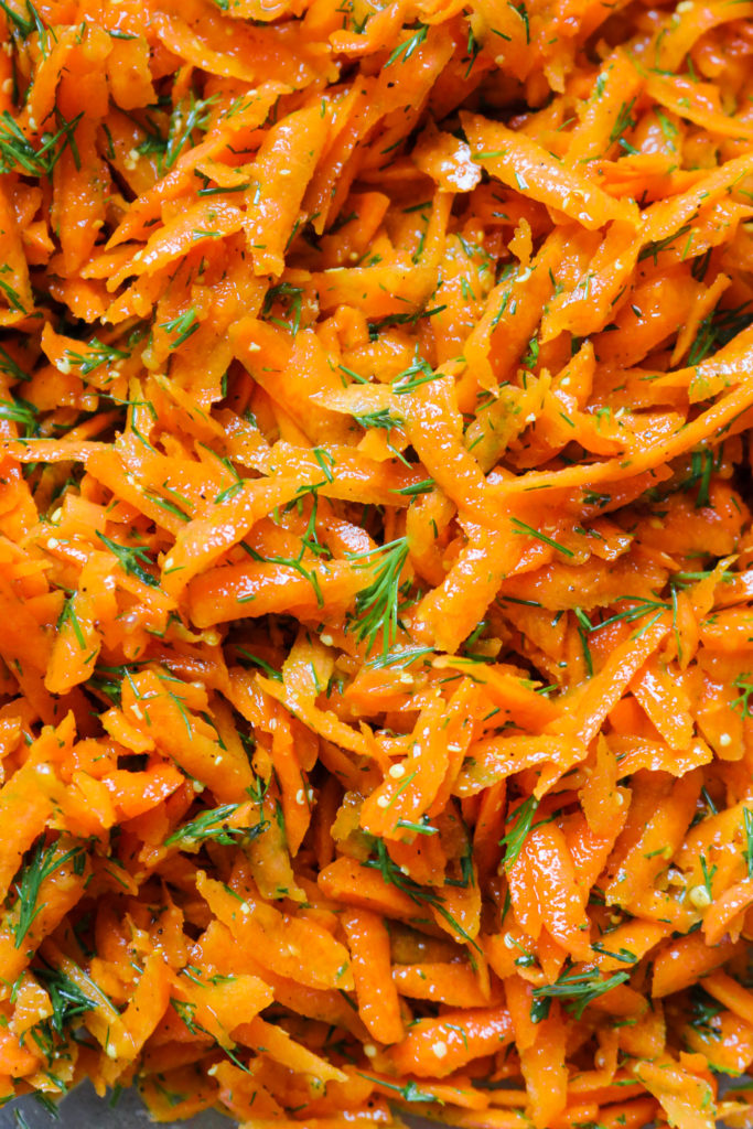 close up shot of shredded carrots with flakes of fresh dill and mustard seeds
