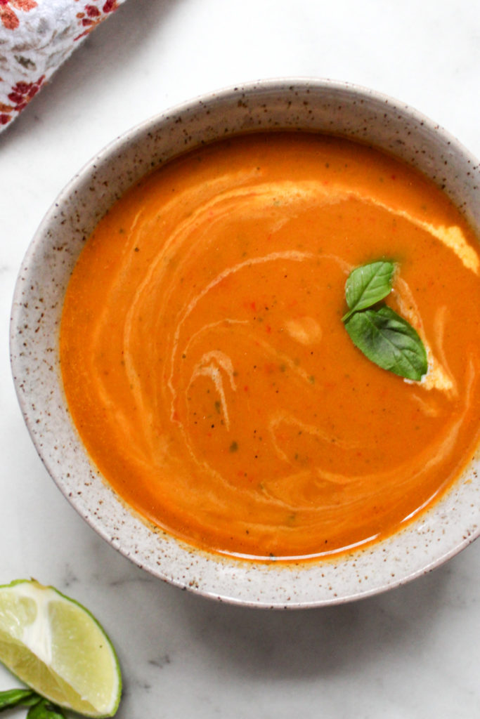 vibrant orange Thai squash soup in a speckled bowl, topped with basil leaves alongside a slice of lime