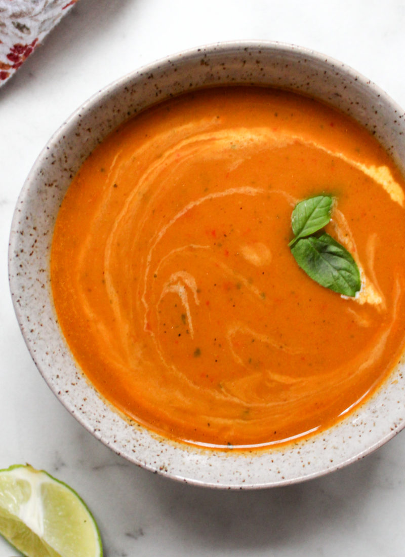 vibrant orange Thai squash soup in a speckled bowl, topped with basil leaves alongside a slice of lime