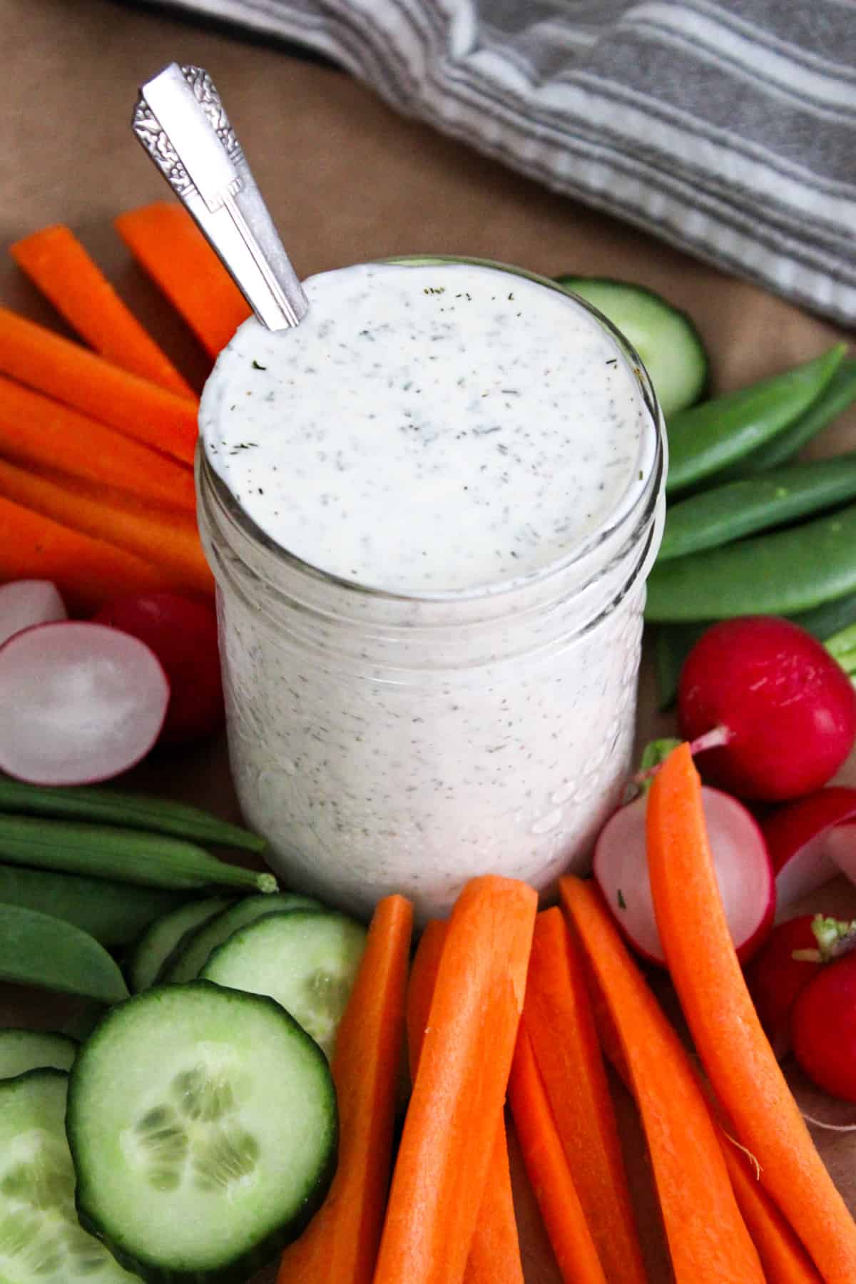 dill pickle ranch dressing in a mason jar with a spoon, surrounded by a rainbow of vegetables