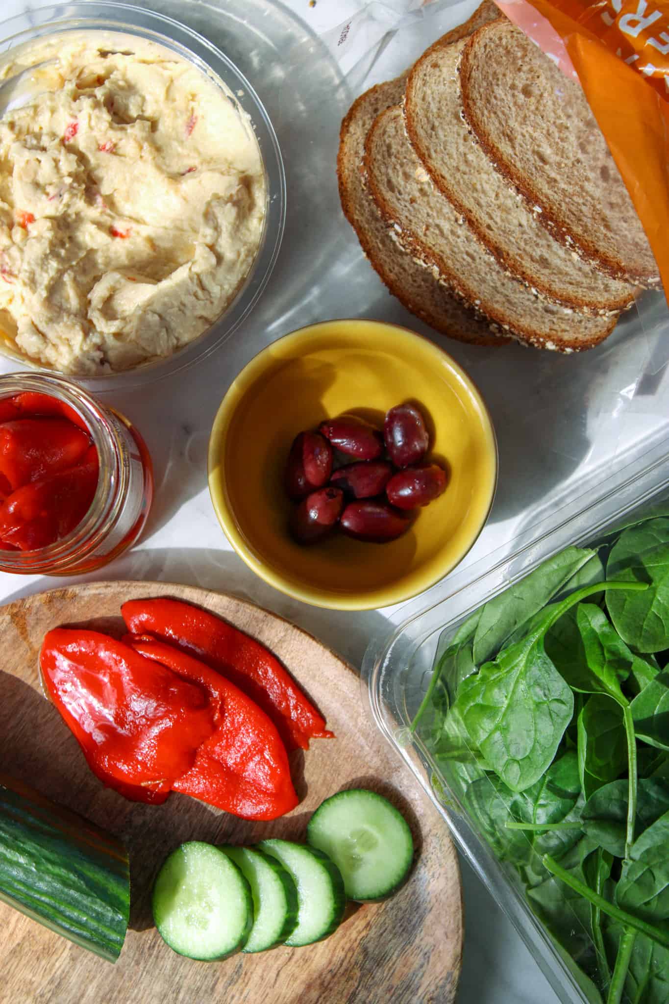 ingredients for mediterranean veggie sandwich with hummus placed on a marble counter