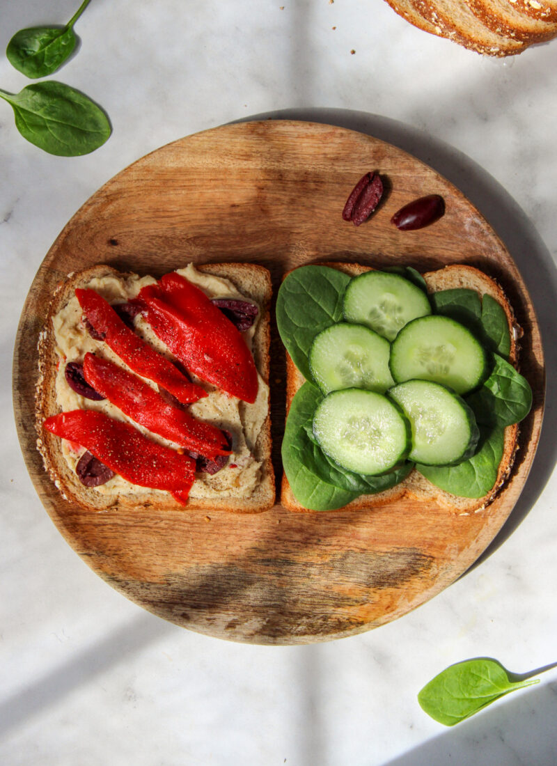 two halves of a mediterranean veggie sandwich on a round wooden plate