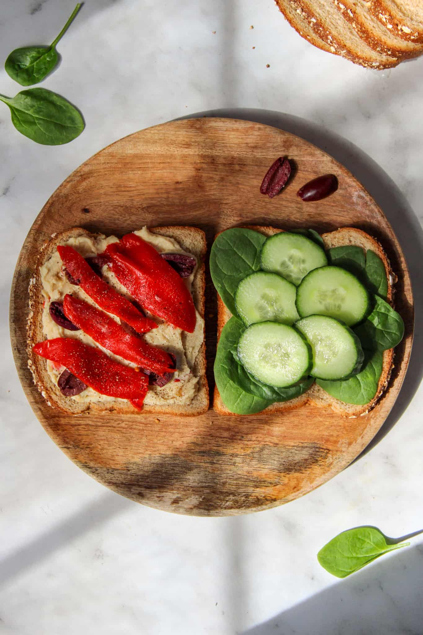 two halves of a mediterranean veggie sandwich on a round wooden plate