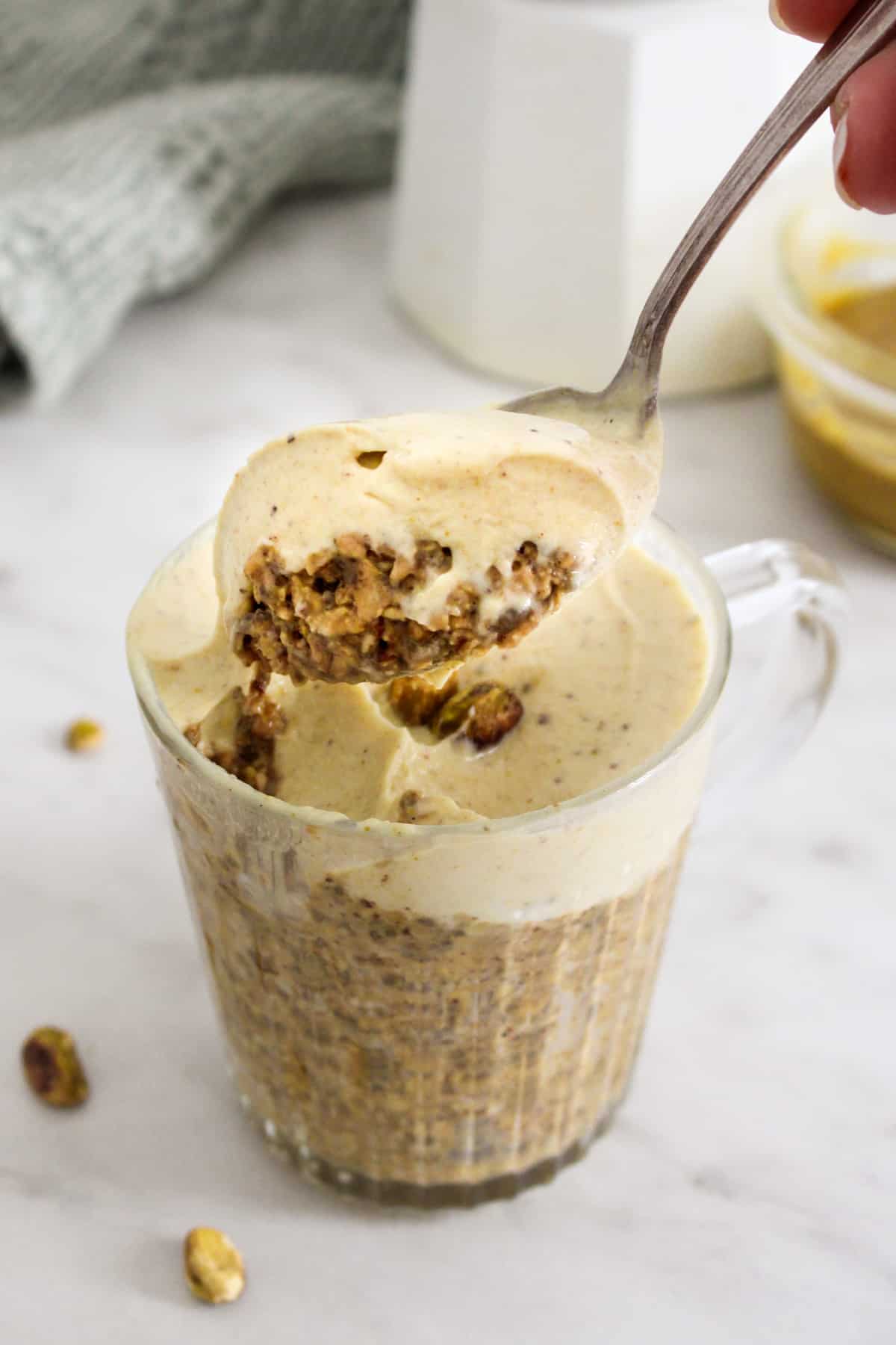 hand holding a metal spoon lifting a spoonful of pistachio overnight oats out of a glass mug