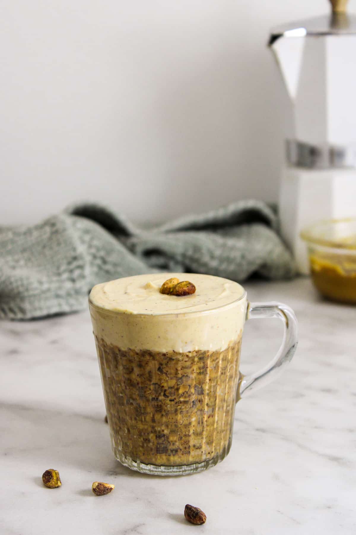 small glass mug containing pistachio oats topped with pistachio yogurt and two pistachios