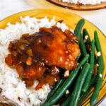 chicken thigh glazed with apricot sauce on a bed of white rice and green beans, served on a retro brown glass plate