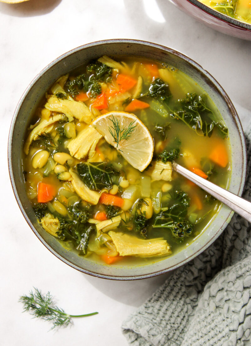 lemon white bean turkey and kale soup in a bowl topped with a lemon slice and dill