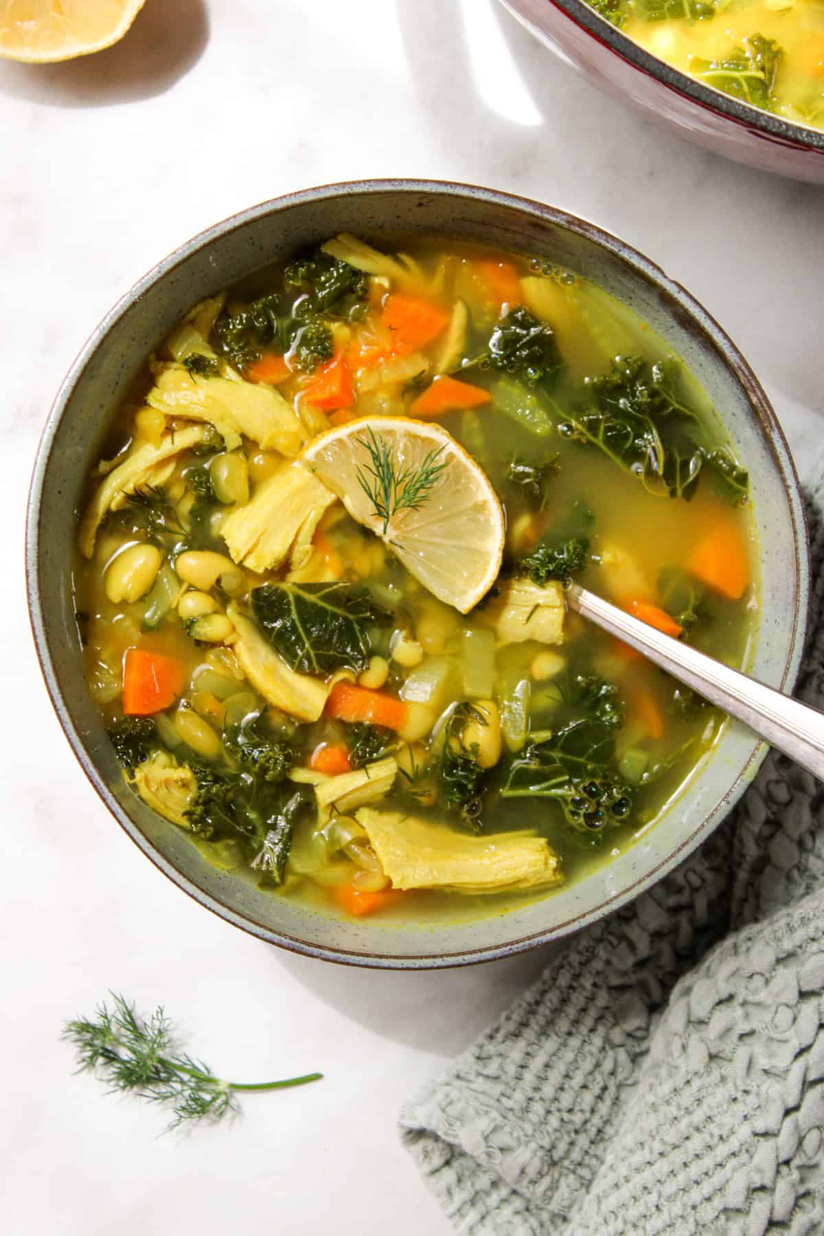 lemon white bean turkey and kale soup in a bowl topped with a lemon slice and dill