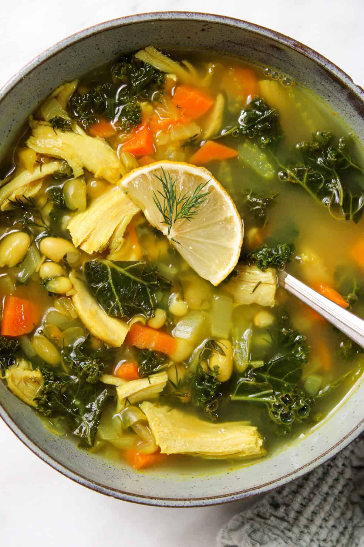 close up of white bean turkey soup in a ceramic bowl topped with a lemon slice