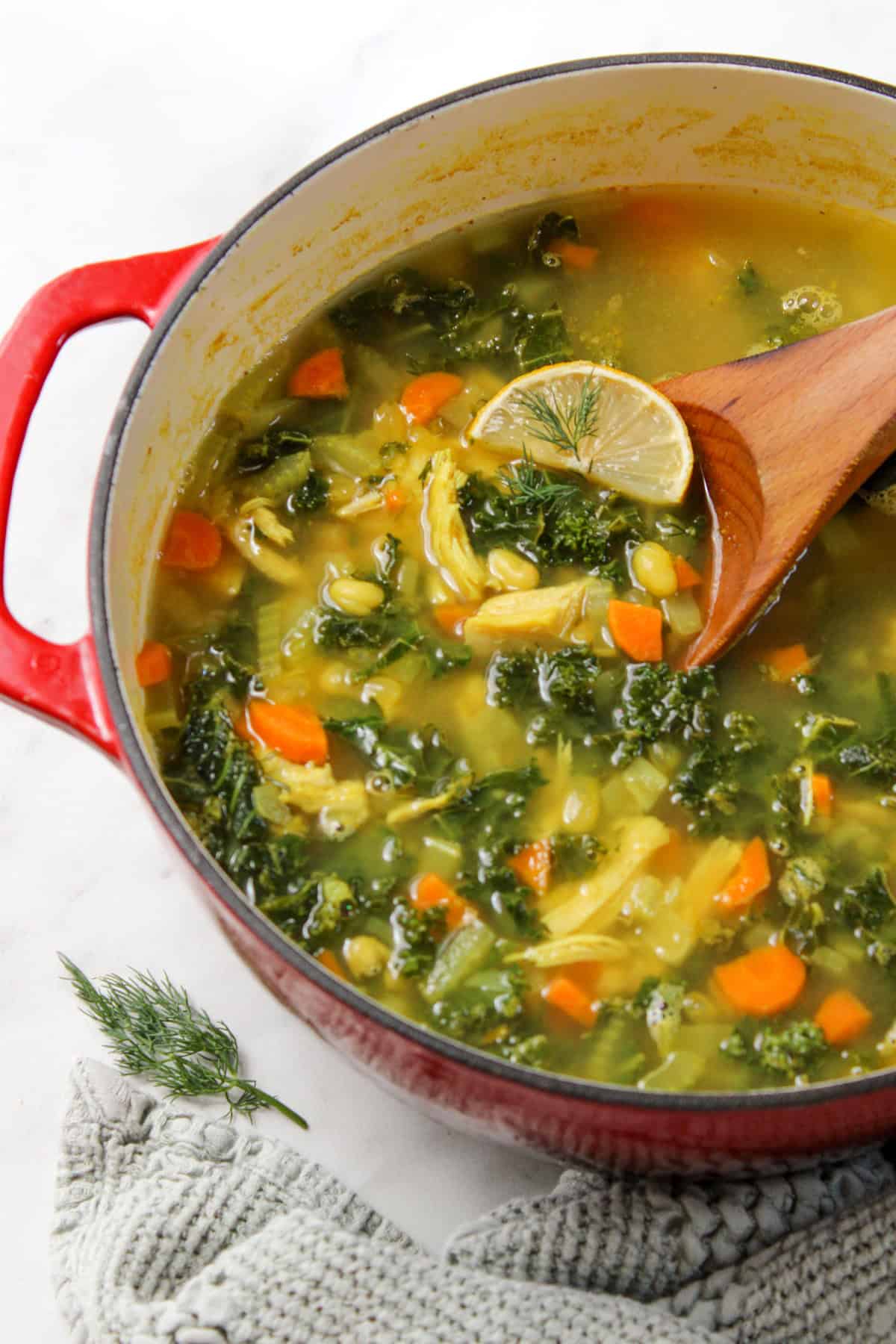 lemony white bean turkey soup in a red pot with a wooden spoon